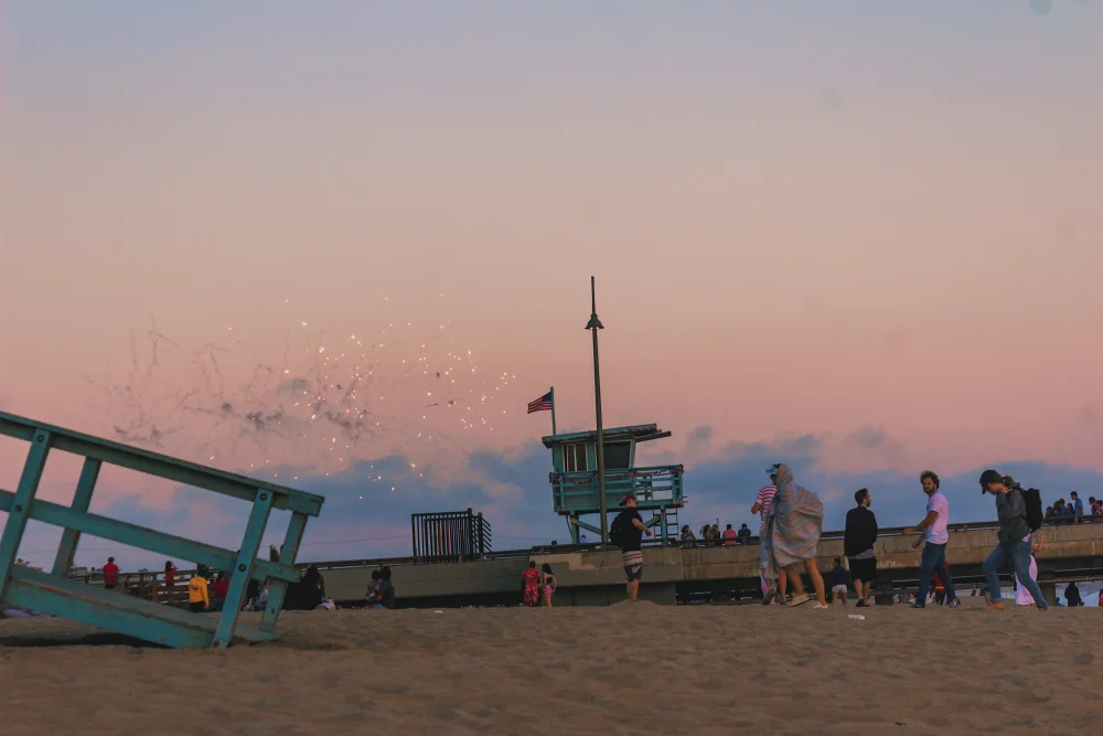 Människor som tittar på fyrverkerier i skymningen från stranden i Los Angeles