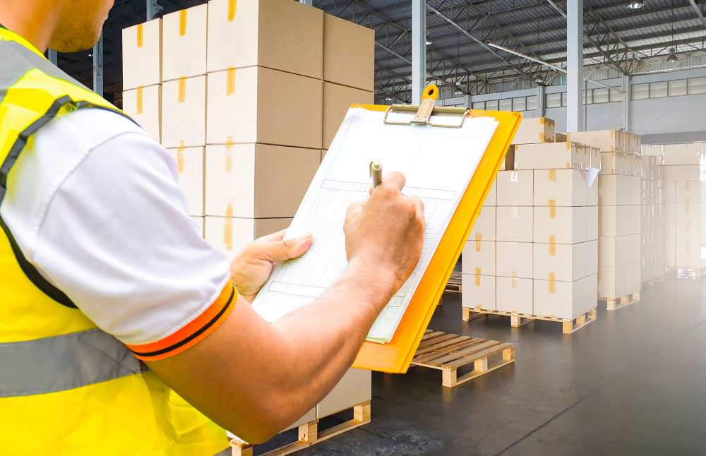 Inspector at a warehouse, holding a clipboard and carrying out a container loading check inspection of packed boxes. 