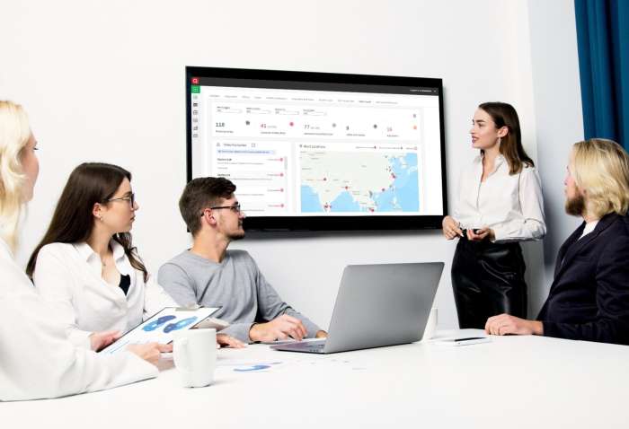 A group of international professionals in a meeting room looking at QIMA Signals dashboard on a TV screen