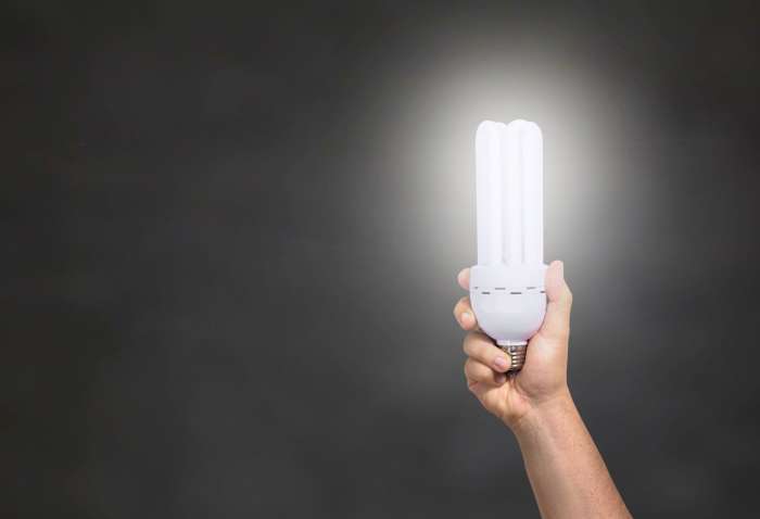 A hand holding up an LED light bulb behind a black backdrop