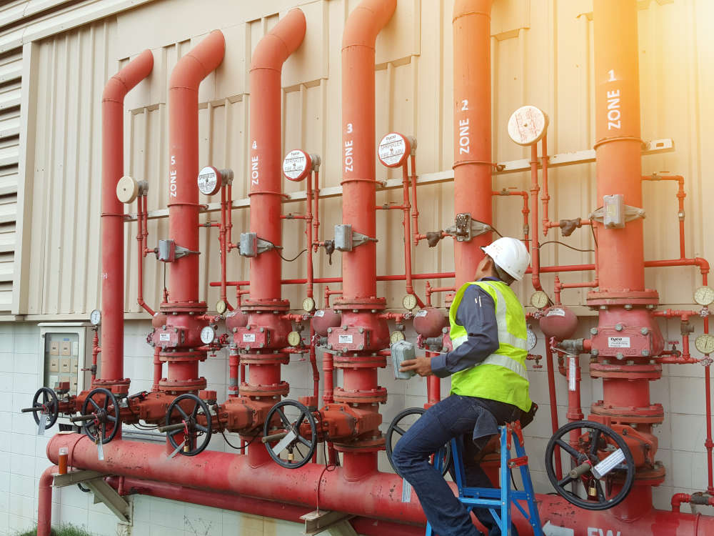 Worker checking structural safety of pipes outside of a building 