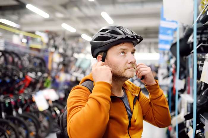 Man in a bike helmet adjusts the straps while shopping in a bicycle store, with bikes visible in the background
