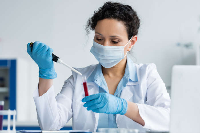 African American scientist in medical mask and latex gloves holding electronic pipette