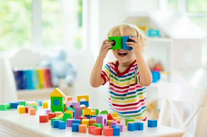 A young child happily playing with colorful blocks in a well-lit room, surrounded by toys and books.