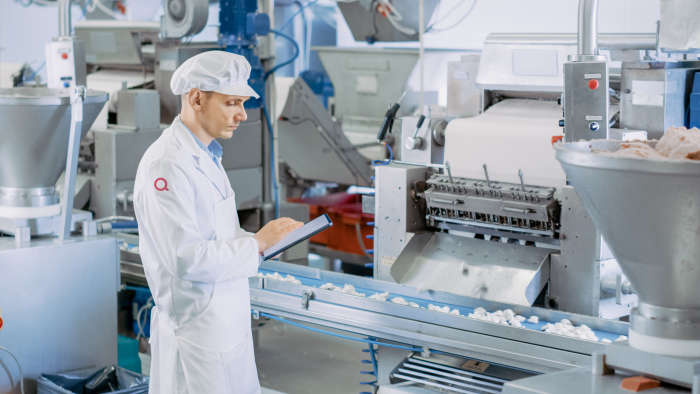 a person in a white lab coat and hat standing in a food factory 
