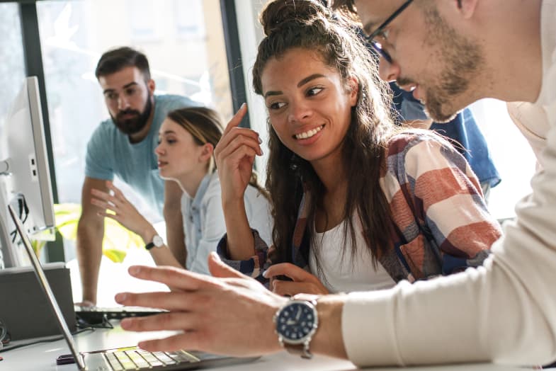 group of young casually dressed colleagues sitting at computers talking