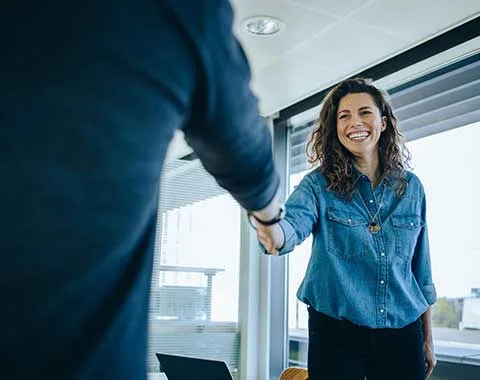 Young white woman smiling shaking hands with person wearing suit who is out of focus off camera