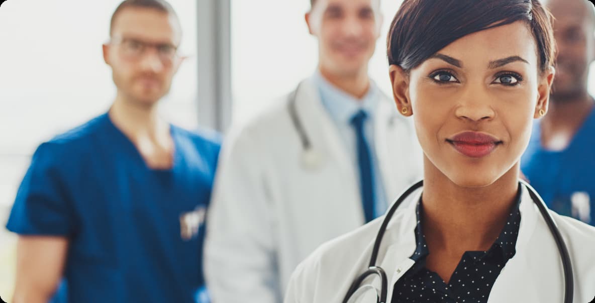 closeup of young female doctor smiling at camera with colleagues behind her out of focus