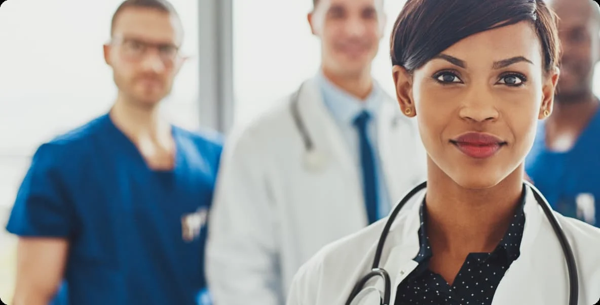closeup of young female doctor smiling at camera with colleagues behind her out of focus