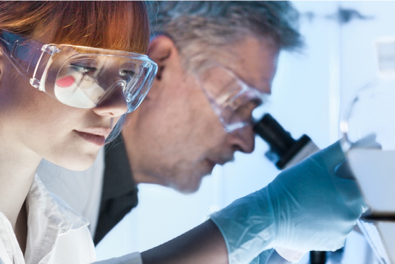 Two medical researchers wearing goggles looking into microscopes