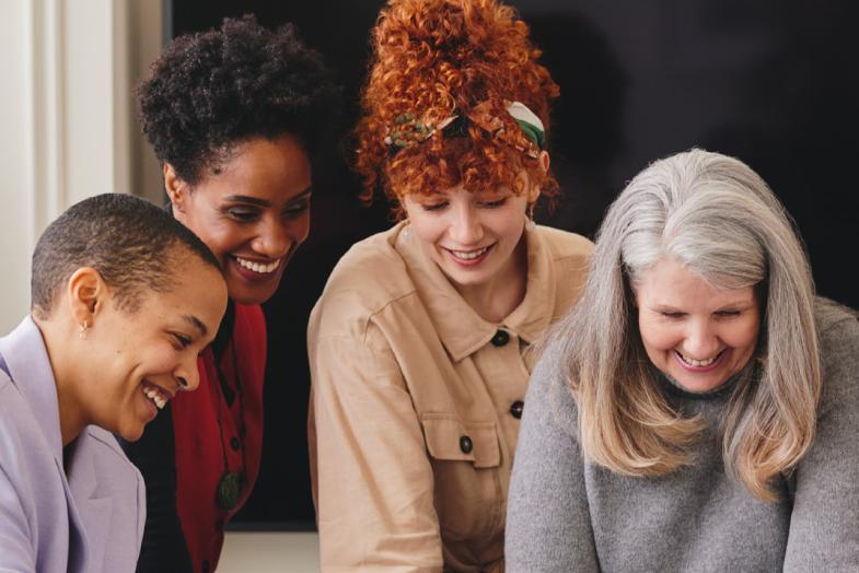 Group of female coworkers huddled together smiling and looking down at a conference table