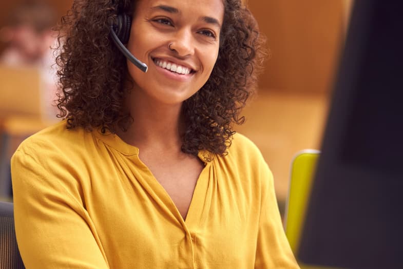 young woman with call headset on smiling looking at desktop computer