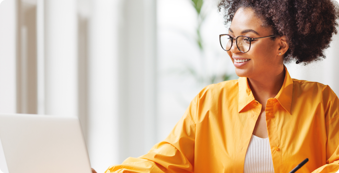 Young woman with glasses and curly hair smiling at computer screen