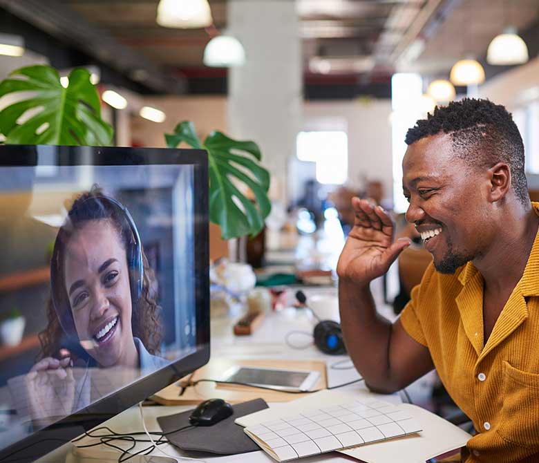 Man sitting at desktop computer, waving at woman on screen