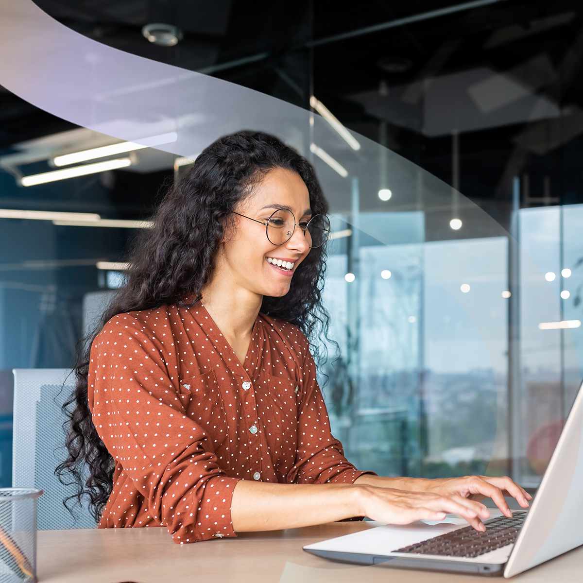 Woman working in office setting sitting at her laptop smiling.