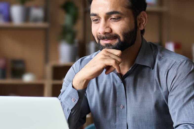 young man in office attire sitting at laptop smiling