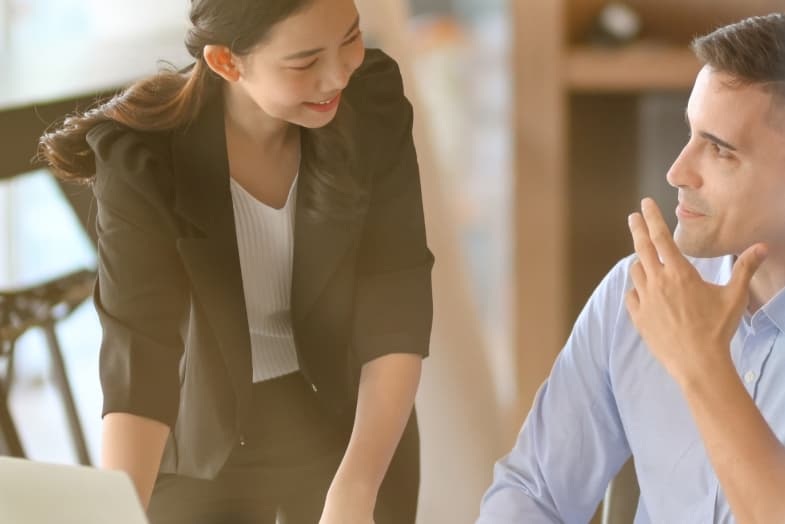 young woman in professional office attire standing next to male coworker smiline