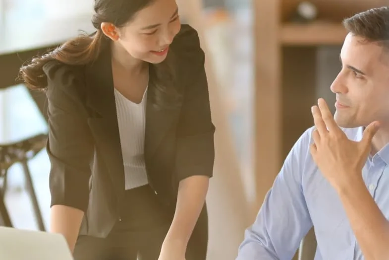 young woman in professional office attire standing next to male coworker smiline