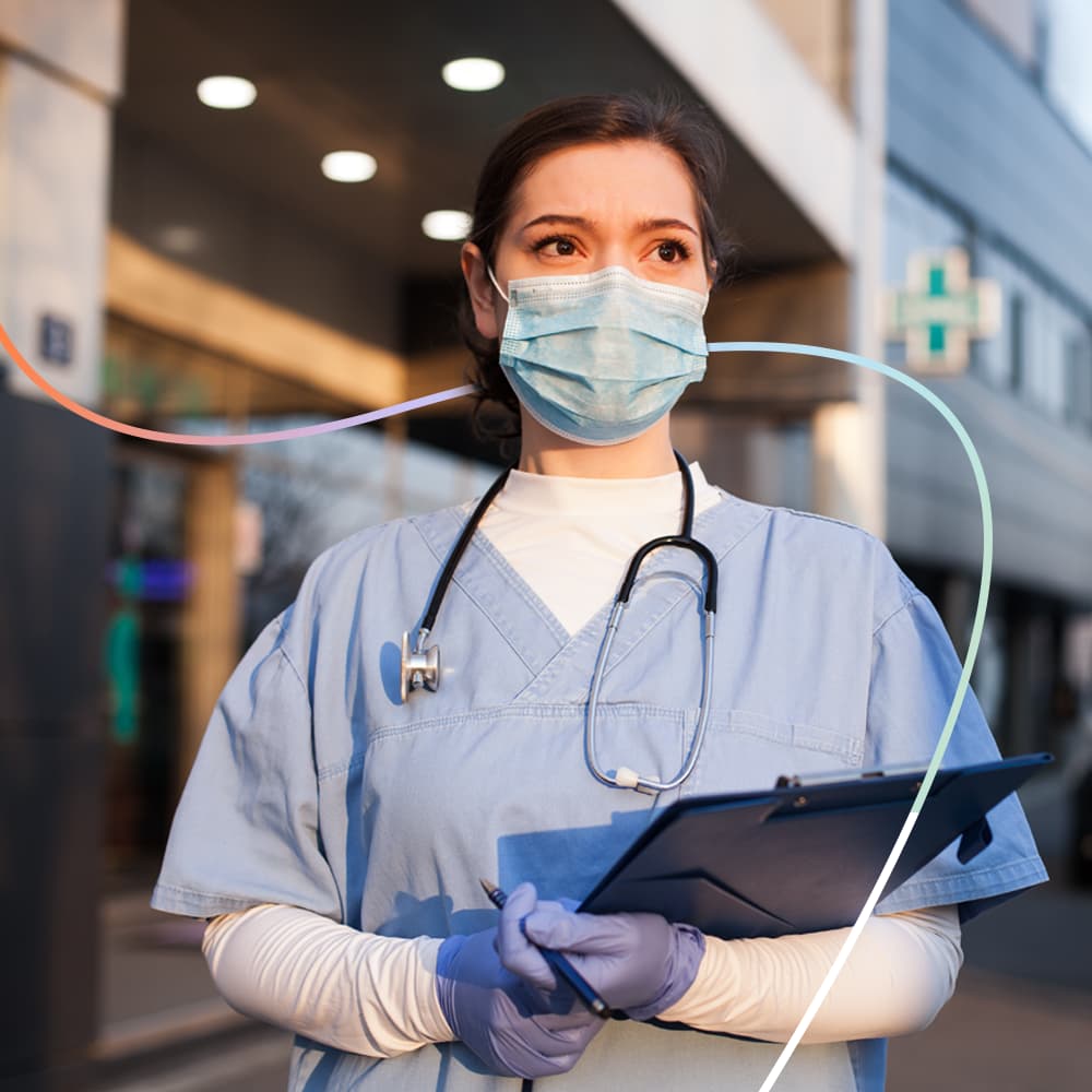 A nurse standing outside a hospital with a clipboard in hand.