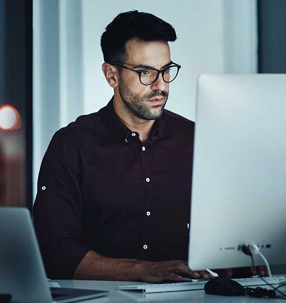 Young white male with glasses, serious expression working at his desktop computer.
