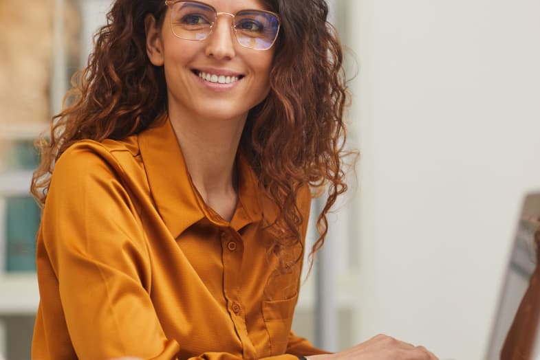 young woman wearing glasses smiling at laptop