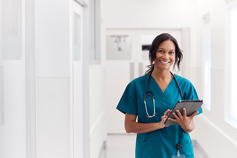 Doctor with stethoscope walking in hallway using a tablet 