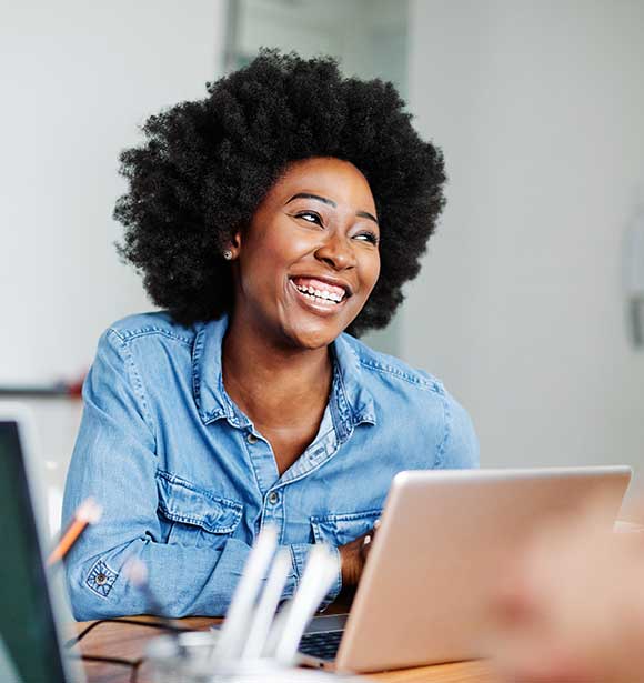 Young black woman smiling, profile view, sitting at laptop.