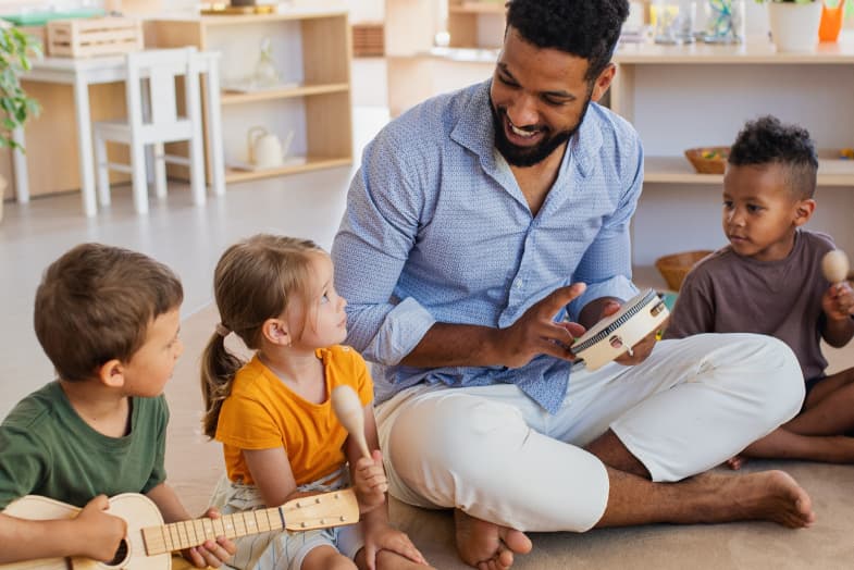 Young male music teacher surrounded by daycare students