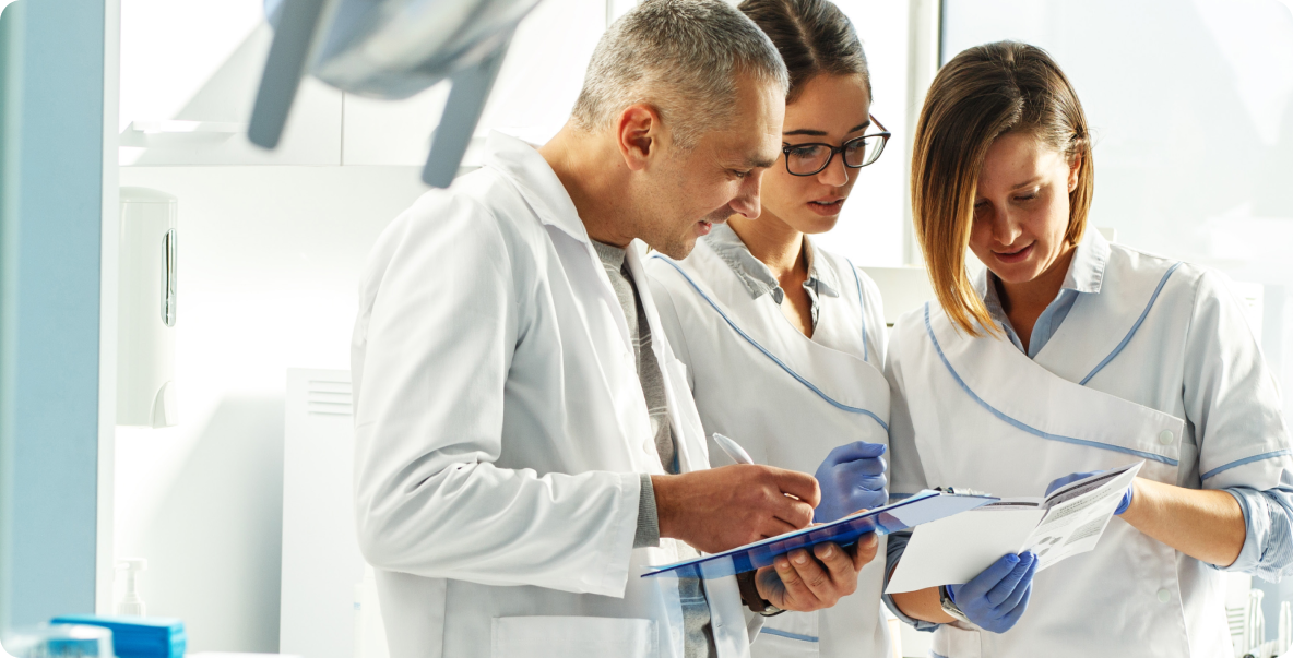 three dental professionals in white suits talking