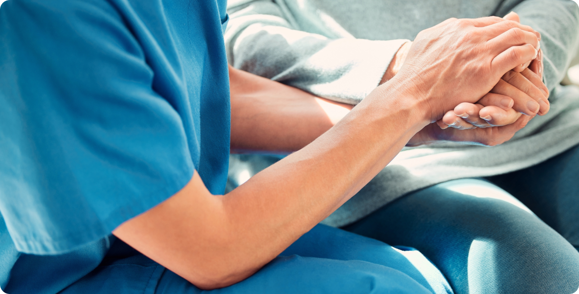 Healthcare worker dressed in scrubs holding older patient's hand