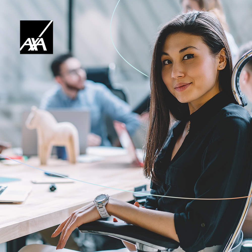 Young woman sitting at office desk, turning to look at camera with soft smile.