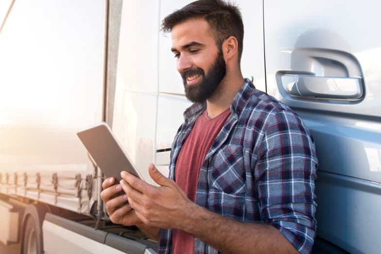 Man wearing flannel shirt using tablet leaning against truck