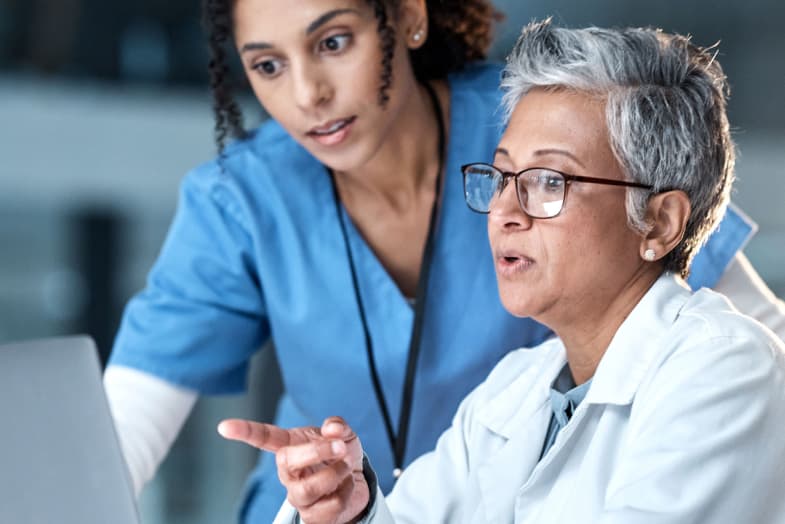 two medical professionals collaborating while sitting at laptop