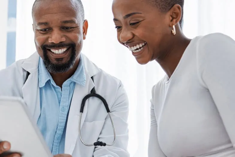 Older doctor sitting with young woman patient smiling at tablet