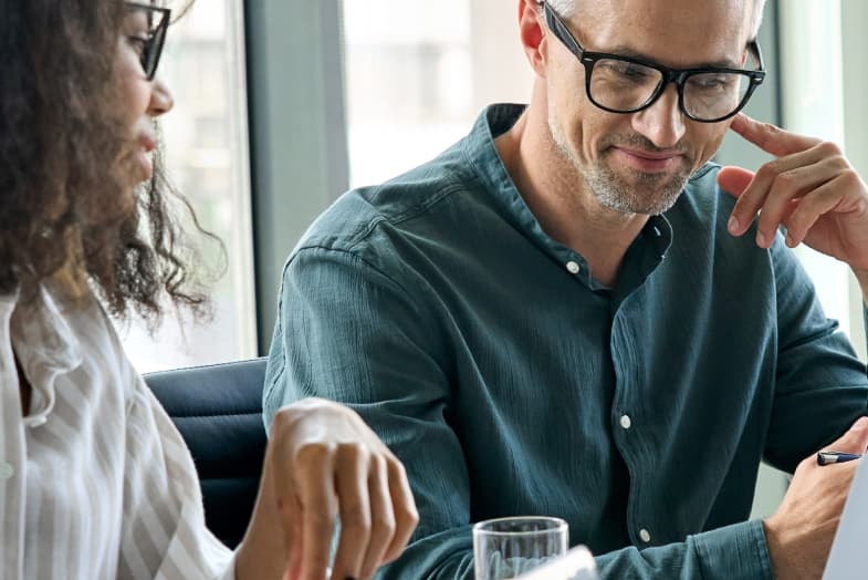 two coworkers sitting at laptop in office setting smiling