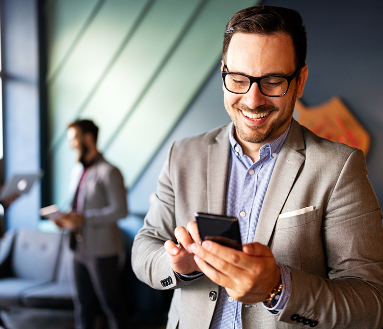 Young male in business suit without tie using smartphone smiling.