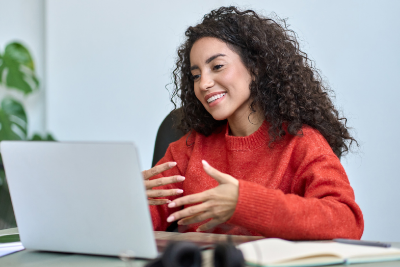 Young woman with curly dark hair smiling and talking on laptop computer