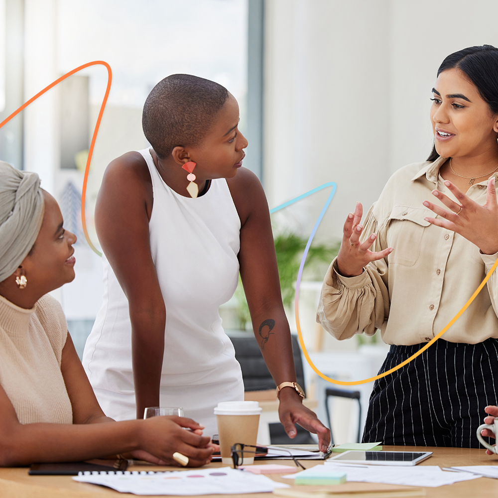 Group of female colleagues standing around table talking.