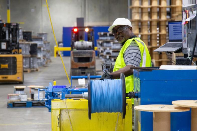 Older male cable worker in factory pulling cable line.