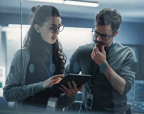 Female office worker showing male coworker information on tablet.