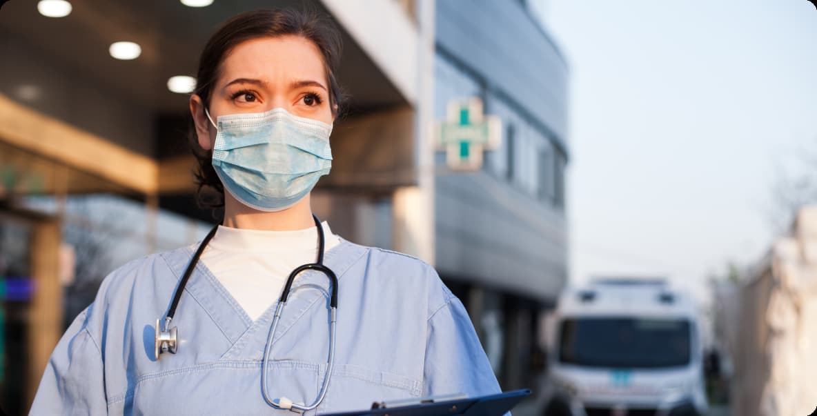 healthcare worker in scrubs standing outside hospital wearing mask