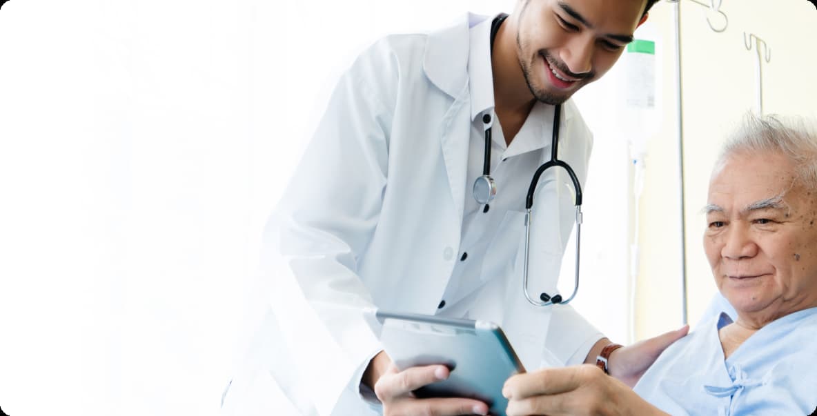 Young asian doctor sitting with older asian patient looking at tablet