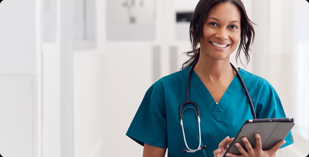 young woman in scrubs smiling with stethoscope and tablet in hand