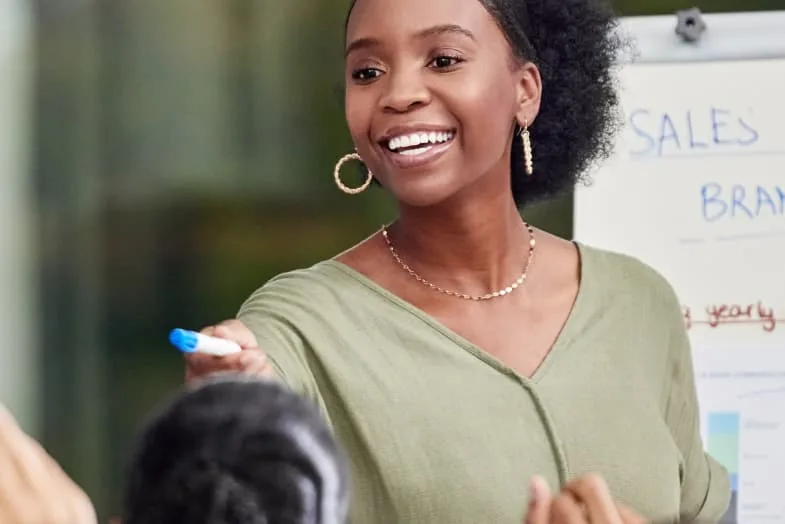 young woman in office setting standing in front of room smiling and pointing with marker