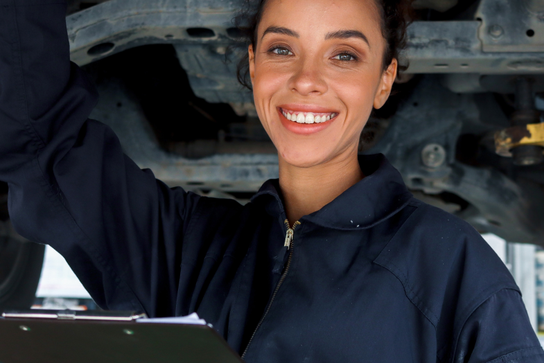 female worker in jumpsuit in front of car at body shop