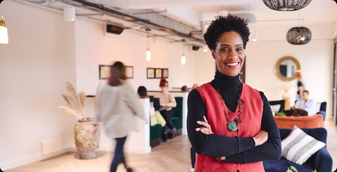 Woman in casual office setting wearing a red vest over black turtleneck with arms crossed smiling