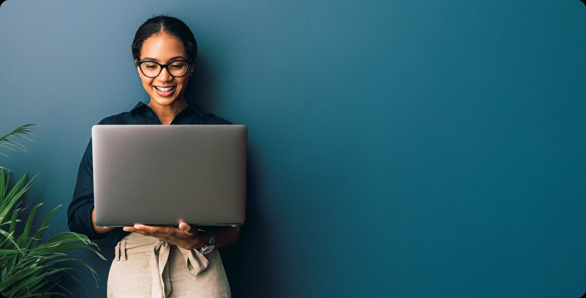 Young woman in office setting standing with laptop open and smiling