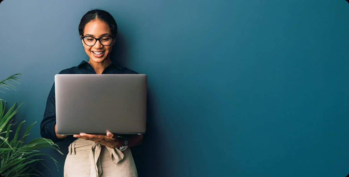 Young woman in office setting standing with laptop open and smiling