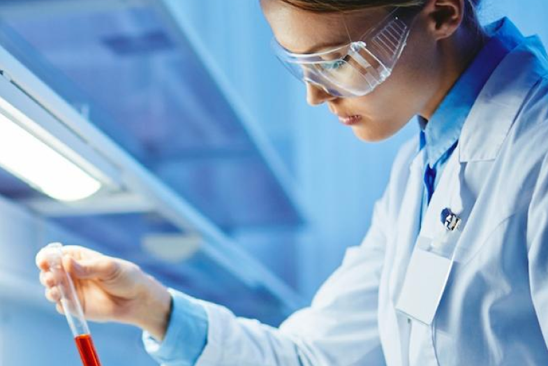 Medical researcher in lab attire looking at test tube