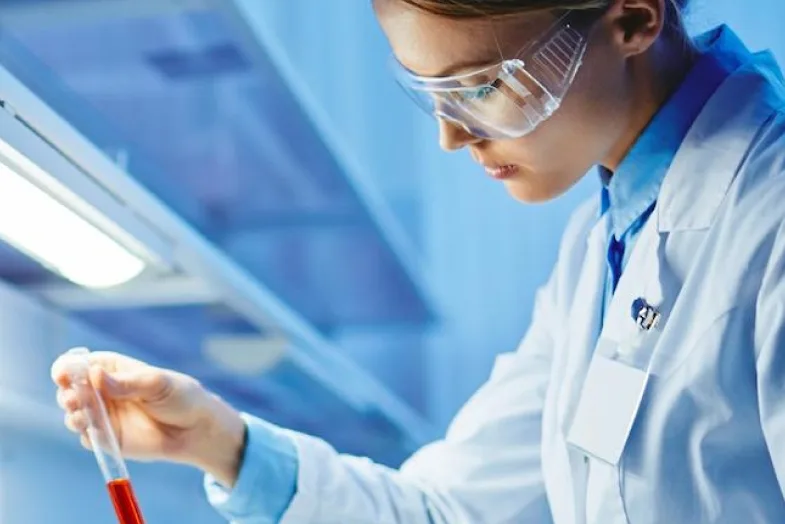 Medical researcher in lab attire looking at test tube